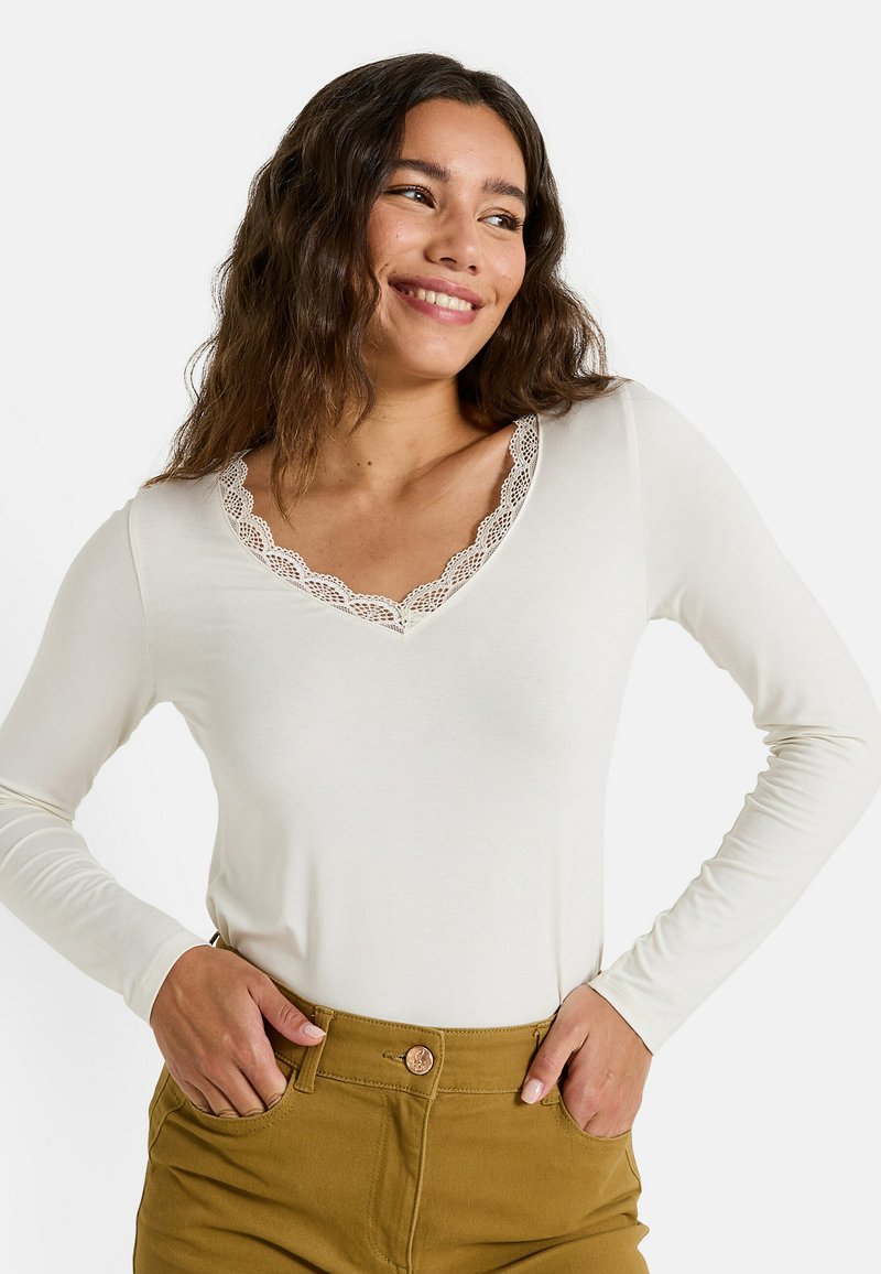 Top de manga larga color crema con escote en V decorado con encaje, hecho de una tela suave; combinado con pantalones marrones de tiro alto.