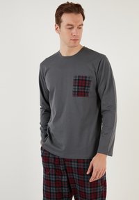 Camisa de manga larga gris con un bolsillo de cuadros, combinada con pantalones de cuadros en tonos rojos y marinos, con un corte relajado y una textura suave.