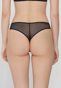 Sous-vêtements hipster en mesh noir avec une taille douce, des coutures lisses et une couverture minimale. Texture de tissu légère et transparente.