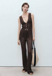 Costum două piese tricotat maro, cu top fără mâneci și decolteu adânc în V, și pantaloni asortați. Țesătura are un model texturat. Include o geantă.