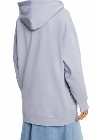 Persona vistiendo una sudadera oversized de color púrpura claro con la capucha puesta, combinada con una falda de mezclilla azul clara, vista desde atrás.