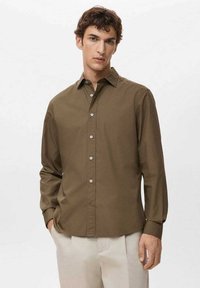 Camisa marrón de botones con mangas largas, que presenta un cuello clásico y una tapeta de botones, hecha de una tela suave, combinada con pantalones beige claro.