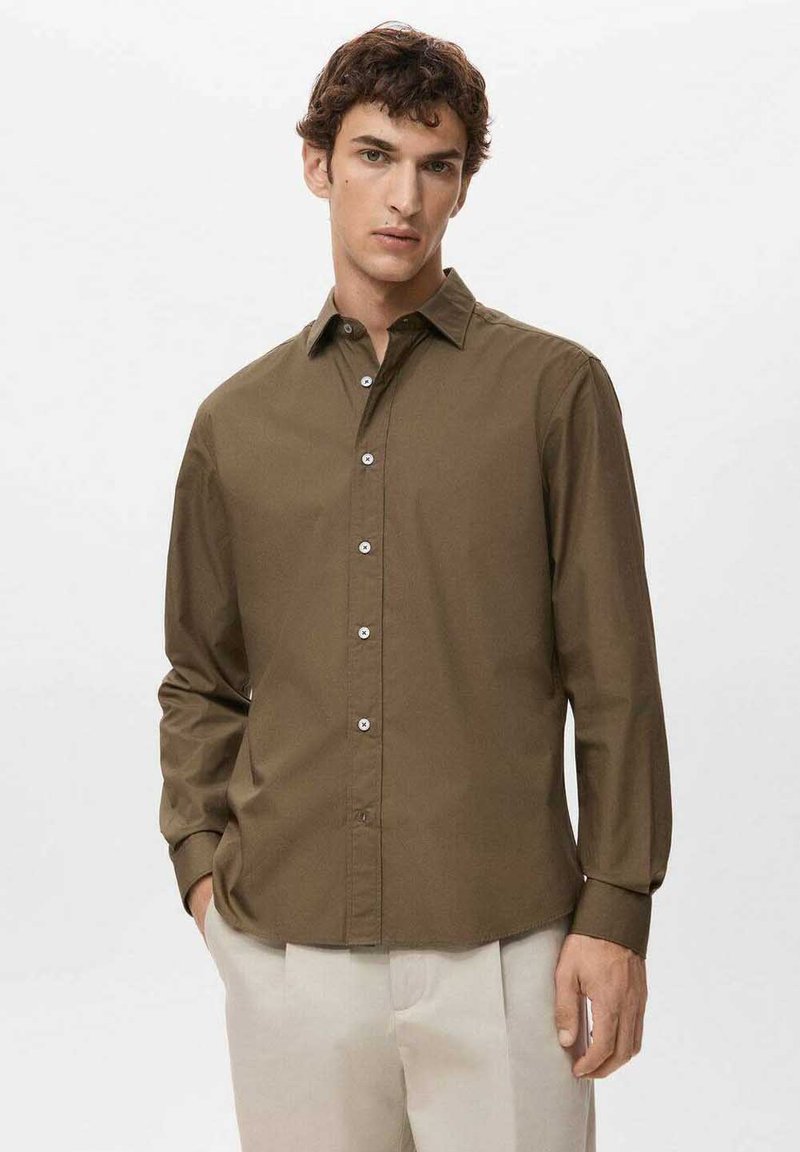 Camisa marrón de botones con mangas largas, que presenta un cuello clásico y una tapeta de botones, hecha de una tela suave, combinada con pantalones beige claro.