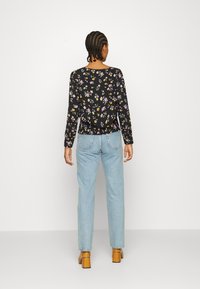 Svart blommig långärmad topp med flerfärgade blommor, matchad med ljusblå raka jeans och bruna klackskor.