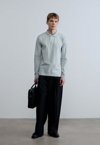 Ανοιχτό γκρι πλεκτό μπλουζάκι με μακριά μανίκια και γιακά, συνδυασμένο με φαρδιά μαύρη παντελόνια και κρατώντας μια μαύρη δερμάτινη τσάντα.