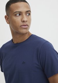 Marineblå bomull t-skjorte med korte ermer, rund hals, med en diskret brodert logo på venstre bryst. Glatt tekstur.