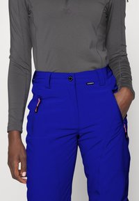 Pantalons de plein air bleus en tissu léger, dotés d'une poche zippée avec des accessoires roses, d'un bouton à la ceinture et d'une coupe fuselée.