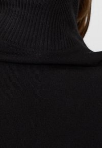 Czarny dzianinowy sweter z wysokim ribbowanym kołnierzem, pokazany z tyłu. Tkanina ma gładką, miękką fakturę i dopasowany krój.