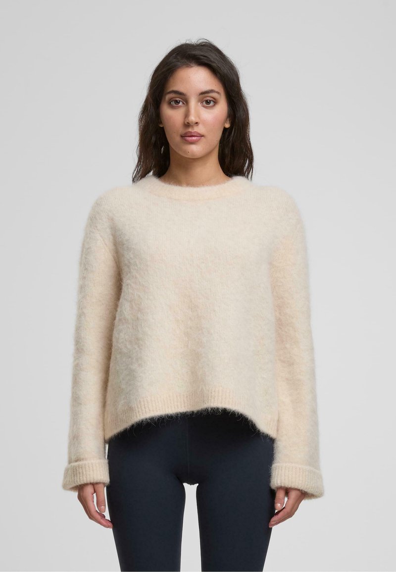 Hellbeige, flauschiger Pullover mit Rundhalsausschnitt, überschnittenen Schultern und gerippten Bündchen. Der Saum ist hinten etwas länger.