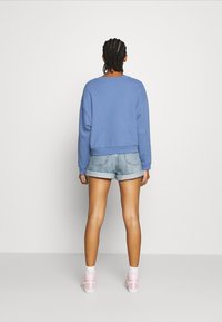 Sudadera azul recortada con mangas largas, combinada con pantalones cortos de mezclilla claros y zapatillas de deporte altas rosas. Diseño simple, ajuste casual.