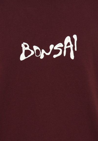 Bordo T-krekls, izgatavots no kokvilnas, ar baltiem rokraksta dizaina burtiem, kas lasāmi kā "BONSAI" dažādās biezumos.