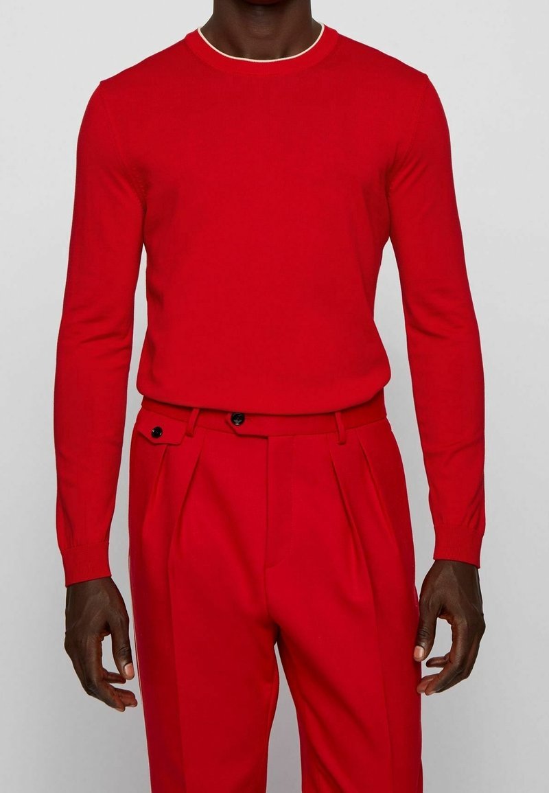 Maglione lavorato a maglia rosso con scollo tondo e maniche lunghe, abbinato a pantaloni rossi su misura con vita alta e pieghe frontali.