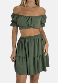 Conjunto verde de dos piezas que incluye un top corto sin hombros con mangas abullonadas y una falda de volantes con cintura elástica. Tela texturizada.