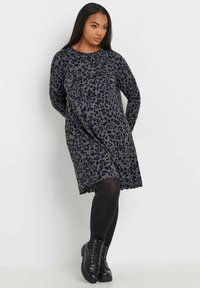 Leopardenmuster-Kleid in Grau-, Schwarz- und Blautönen, mit langen Ärmeln und lockerer Passform. Kombiniert mit schwarzen Schnürstiefeln und Strumpfhosen.