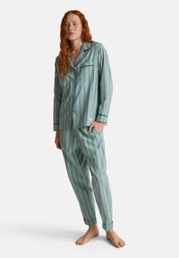 Gestreept pyjama set in lichtblauw en groen. Bevat een button-up shirt met zak, lange mouwen en omgeslagen broekspijpen. Zachte stoffen textuur.
