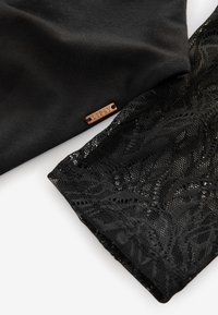 Černá látka s malou měděnou štítkem označenou "Lipsy", vedle černé krajkové látky s květinovým vzorem na bílém pozadí.