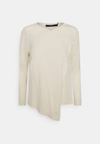 Krémově zbarvený top s dlouhým rukávem s překříženým designem, výstřihem do V a asymetrickým lemem. Měkká textura s pružným materiálem.