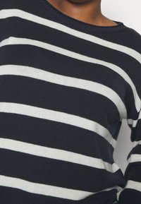 Maglione blu navy con strisce bianche orizzontali, scollatura rotonda, texture morbida e un piccolo logo in basso a sinistra.