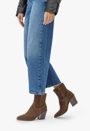 Braune Wildleder-Ankle-Boots mit einer spitzen Zehenpartie, dekorativen Nähten und einem seitlichen Reißverschluss, kombiniert mit weit geschnittenen blauen Jeans.
