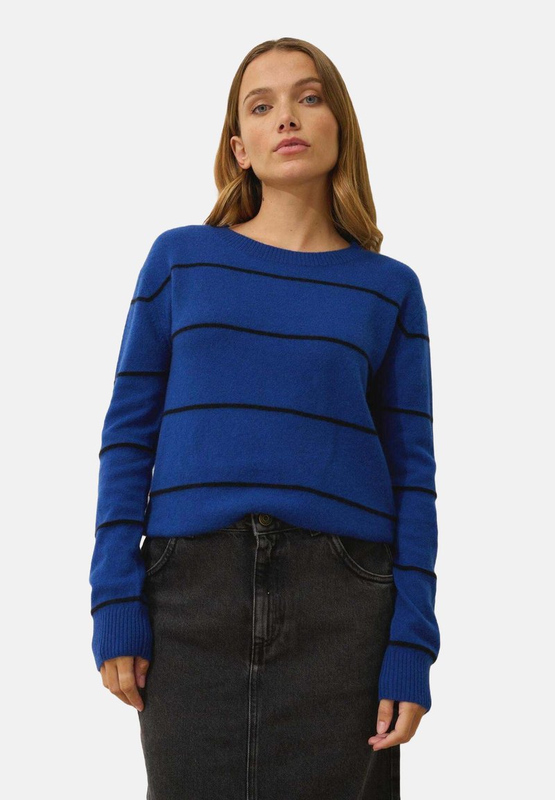 Blå stickad tröja med svarta horisontella ränder, rund halsringning och ribbade ärmslut, tillsammans med en mörk denimkjol.