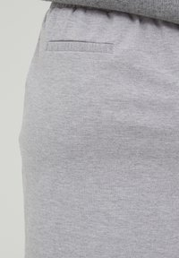 Pantalons de survêtement en coton gris avec une texture douce, dotés d'une taille élastique et d'une seule poche arrière. Design simple et décontracté.
