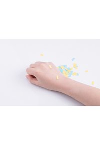 En ljus hudfärgad hand vilar på en yta med utspridda blå och gula fyrkantiga konfettibit. Händerna är släta med en oputsad yta.