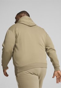 Felpa beige con una finitura testurizzata, dotata di cappuccio con coulisse e polsini a costina. Il design è semplice, con una vestibilità rilassata e dettagli minimi.