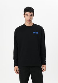 Black long-sleeve t-shirt made of cotton, featuring a blue "Hugo" logo on the left chest area. Simple design with crew neckline.