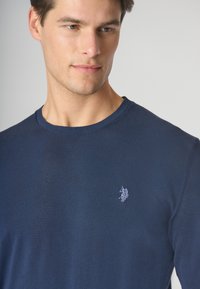 Maglietta a maniche lunghe blu navy in un tessuto texturizzato, con collo a giro, caratterizzata da un piccolo logo ricamato bianco sul lato sinistro del petto.