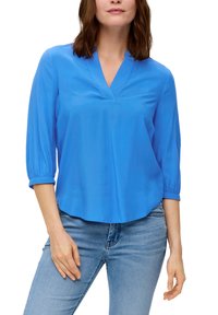 Blauwe, lichte blouse met een v-hals, driekwart mouwen en een ontspannen pasvorm. Soepele textuur en gebogen zoom, gecombineerd met lichtblauwe jeans.