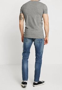 Grå t-shirt med korta ärmar tillsammans med blå jeans i denim. T-shirten har en rund halsringning; jeansen har en klassisk passform med diskret blekning. Svarta skor.
