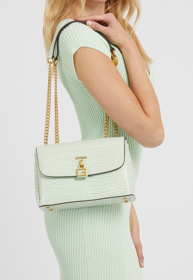 Mátově zelená kabelka z umělé kůže s krokodýlovým embosováním, se zlatými detaily, řetízkovým popruhem a černými prvky. Má klopový uzávěr a logo detail.