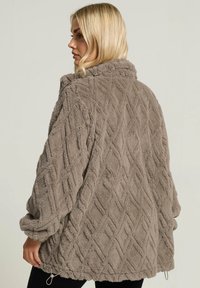 Chaqueta borrosa de color topo hecha de tejido texturizado, con un patrón de diamantes y un cordón en el dobladillo para ajustar.