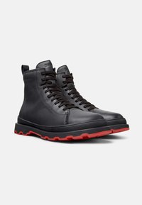 Black leather ankle boots with black laces and a red rubber sole, displayed against a white background.