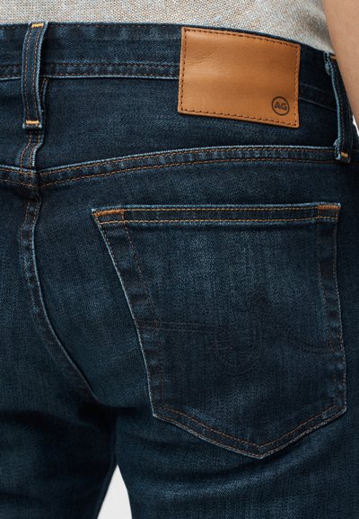 Σκούρο μπλε τζιν με δερμάτινο ταμπελάκι στο περίζωμα, πορτοκαλί ραφές και πίσω τσέπη με διακριτικές λεπτομέρειες.