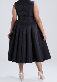 Svart satindress med figursydd liv och utsvängd kjol, med en dold dragkedja bak. Bärs med nude högklackade skor.