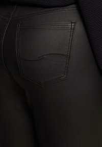Zwarte denim jeans met een soepele textuur, voorzien van een achterzak met subtiele stiksels en een slanke, getailleerde pasvorm.