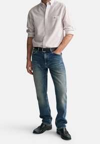 Man med uppvikt rutig skjorta, blå urtvättade jeans, svart bälte och svarta loafers, står med ena handen i fickan.