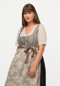 Schwarz-weiß gemustertes Kleid mit einer Spitzenüberlagerung. Es hat ein transparentes weißes Oberteil mit kurzen Ärmeln und ein braunes Satinschleifenband in der Taille.