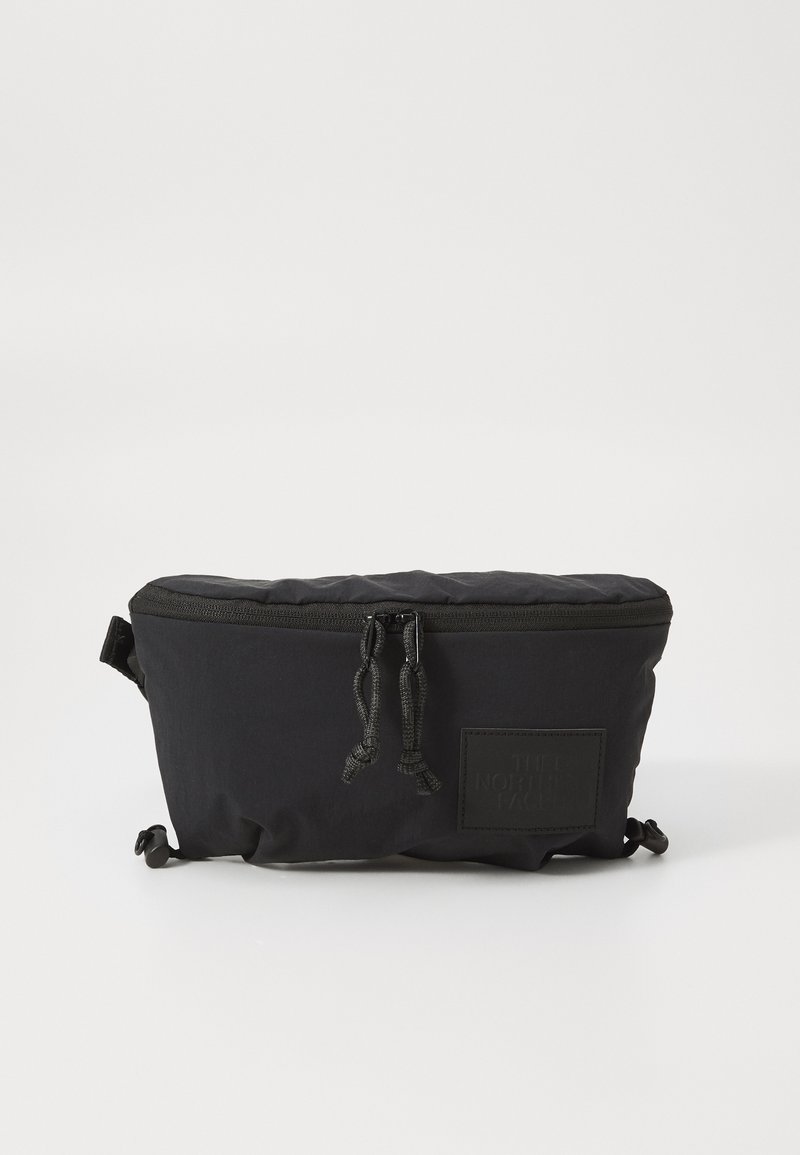 Black zippered bag made of soft fabric, featuring a quilted upper, adjustable drawstring closures, and a branded patch on the front.