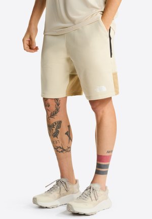 Beige athletic shorts made of lightweight fabric with a textured patch on the side; features a black zipper pocket. Brand logo on the hem.