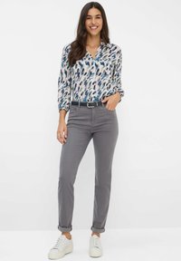 Blusa a maniche lunghe con motivi di foglie multicolori, abbinata a pantaloni grigi a sigaretta e sneakers bianche, con una cintura nera.