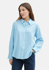 Camicia button-up a righe blu chiaro, con colletto, maniche lunghe e vestibilità rilassata. Tessuto texture, strisce bianche a contrasto e bottoni visibili.