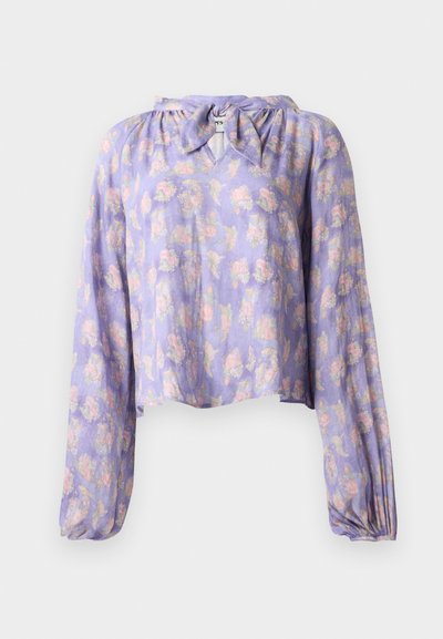 Bluză florală dintr-un material violet deschis, cu mânecă lungă bufantă și decolteu legat. Prezintă un imprimeu delicat cu flori roz și verzi.