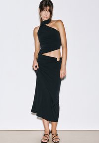 Schwarzes Zwei-Teile-Outfit mit einem Trägershirt in asymmetrischem Design und einem Midirock mit Ausschnittdetails an der Taille.