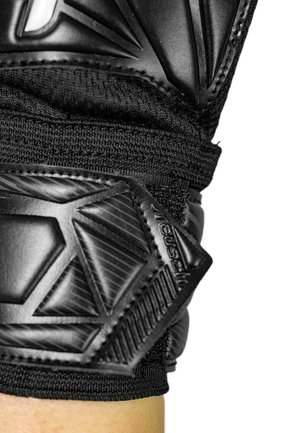 Close-up of a black padded glove wrist strap with textured rubber and fabric materials securing the glove on a light-skinned arm.