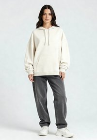 Kreemist kapuutsiga pusa koos kenguru-taskuga, reguleeritava kapuutsi ja ribadega varrukatega, koos hallide avarate teksade ja valgete tossudega.