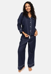 Marineblauw pyjama set in zachte stof met lange mouwen, knoopsluiting aan de voorkant en contrasterende witte bies op de kraag en manchetten, met wijd-uitlopende broekspijpen.