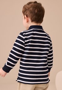 Detská polokošeľa s dlhým rukávom v námorníckych modrých a bielych pruhovaných farbách, s golierom, bočnými rozparkami a rebrovanými manžetami, zobrazená zozadu.