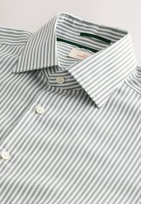 Zeleno-bíle pruhovaná košile s límečkem na knoflíky, obsahující bílé knoflíky a hladkou bavlněnou texturu. Štítek uvnitř límce.